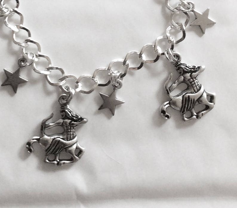 Op de afbeelding: Een zilveren armband met een zilveren ketting en meerdere bedels. De bedels zijn een ster en een centaurfiguur.