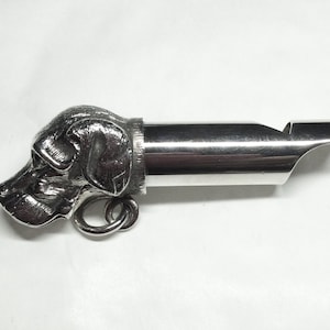 May include: Silver whistle with a detailed dog head design. The whistle has a ring for attaching to a keychain or lanyard.