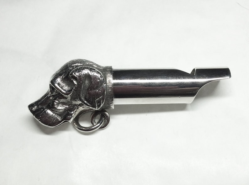 May include: Silver whistle with a detailed dog head design. The whistle has a ring for attaching to a keychain or lanyard.