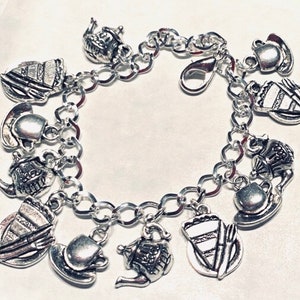May include: Silver charm bracelet with tea party-themed charms. Charms include teapots, teacups, saucers, and cake slices. The bracelet has a lobster clasp and is made of linked chain.