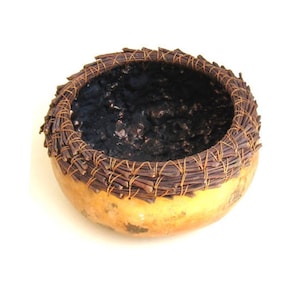 May include: A small, round, woven gourd bowl with a dark brown rim and a black interior. The bowl is made of natural materials and has a rustic, handcrafted look.