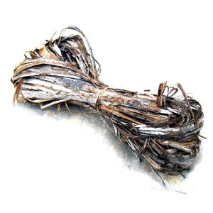 May include: A bundle of dried, natural-colored plant fibers tied with a thin, light-brown twine. The fibers are a mix of brown, gray, and white, with a rough, textured appearance. The bundle is tightly wound.