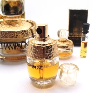 May include: Several perfume bottles are displayed, showcasing a variety of designs. The bottles have gold-colored accents and are filled with a yellow liquid. One bottle is labeled "CHAMPAGNE," while another is labeled "YVES SAINT LAURENT."