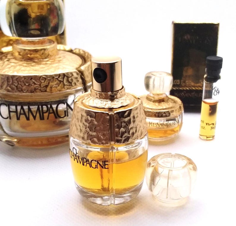 May include: Several perfume bottles are displayed, showcasing a variety of designs. The bottles have gold-colored accents and are filled with a yellow liquid. One bottle is labeled "CHAMPAGNE," while another is labeled "YVES SAINT LAURENT."
