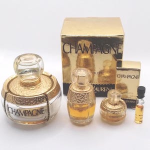 May include: A collection of gold-toned perfume bottles and boxes. The bottles have clear glass stoppers and are labeled "Champagne" and "Yves Saint Laurent". The boxes are gold with the word "Champagne" printed on them.