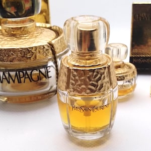 May include: Several miniature perfume bottles with gold accents and clear glass. The bottles have a textured gold top and a clear glass base. The bottles are labeled with the brand name "Yves Saint Laurent" and the word "Champagne".