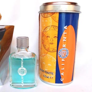 May include: A small glass bottle of turquoise-colored cologne and a cylindrical tin. The bottle and tin feature the text "CALIFORNIA 90210". The tin has a yellow background with sun graphics and a blue and orange stripe.