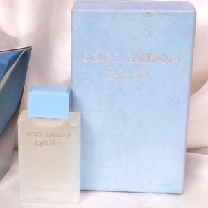 Könnte beinhalten: Eine hellblaue Schachtel und ein Parfümflakon mit den Worten "Dolce & Gabbana Light Blue" aufgedruckt. Der Parfümflakon hat einen hellblauen Deckel und einen transparenten Glaskörper. Die Schachtel ist hellblau.
