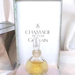 May include: A miniature glass perfume bottle with a teardrop shape and a decorative stopper. The bottle contains a light yellow liquid and is presented in a box with the text "CHAMADE PARFUM GUERLAIN".