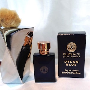 Puede incluir: Un frasco azul oscuro de Versace Dylan Blue Eau de Toilette con tapón dorado y caja negra. La caja tiene letras doradas y un logotipo dorado de cabeza de Medusa. El frasco es de 5 ml.