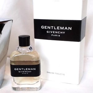 May include: A clear glass bottle of Gentleman Givenchy Eau de Toilette with a black cap and a black label. The bottle is next to a white box with the words "GENTLEMAN GIVENCHY PARIS" in white on a black band.