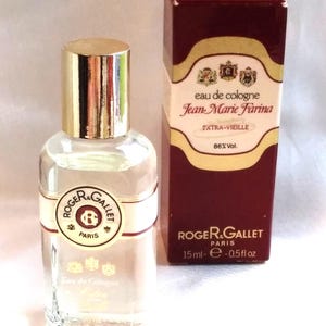 Op de afbeelding: Een heldere glazen fles Roger & Gallet Jean-Marie Farina Eau de Cologne met een gouden dop, naast een bordeauxrode doos. De fles heeft een wit etiket met de merknaam en een cirkelvormig embleem. De doos leest "EXTRA-VIEILLE" en "15 ml".