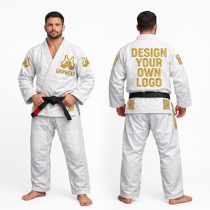Puede incluir: Un kimono de artes marciales blanco con un cinturón negro de punta roja. El frente muestra un logotipo dorado de Gripwear en el pecho y los hombros. La espalda presenta el texto bordado en oro DESIGN YOUR OWN LOGO con detalles dorados en mangas y dobladillo.