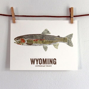 May include: A print of a cutthroat trout made from a collage of maps. The fish is brown, green, and red with a white background. The text "WYOMING CUTTHROAT TROUT" is printed below the fish.