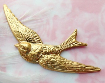 May include: A gold-colored metal bird charm in the shape of a swallow in flight. The bird has detailed wings and a long tail.