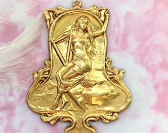 May include: A gold-toned metal pendant featuring a raised relief design of a woman playing a harp. The pendant has an ornate, Art Nouveau style frame.