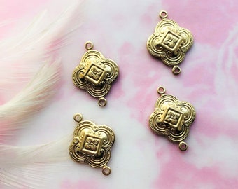 May include: Four gold-tone metal connector charms with an ornate design. Each charm has a square shape with rounded edges and a raised floral pattern in the center. The charms have two jump rings on each side for attaching to jewelry.