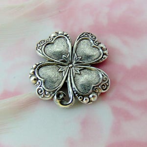 May include: A silver four-leaf clover charm with a detailed design and a textured finish.