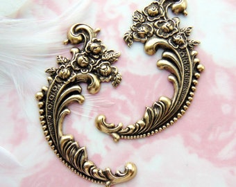 May include: Two ornate gold metal embellishments with a floral design. The embellishments are shaped like a curved scroll with a cluster of roses at the top.