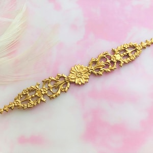 Pode incluir: Moldura decorativa de metal dourado com design floral. A moldura é ornamentada e apresenta um padrão repetitivo de flores e folhas.