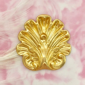 May include: A gold-colored metal decorative accent piece with a fan-shaped design. The piece has a detailed, ornate design with a central floral motif.