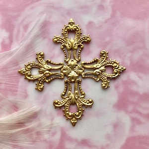 Puede incluir: Una cruz de metal dorado con detalles intrincados y un diseño floral en el centro. La cruz está sobre un fondo rosa y blanco.