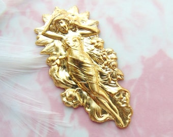 May include: Gold-toned metal charm featuring a stylized figure of a woman with flowing hair and drapery. The charm is detailed with floral accents and has a textured surface.
