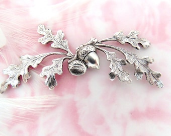 May include: Silver-toned metal acorn charm with detailed oak leaves. The charm features two acorns with a textured surface and a realistic design.