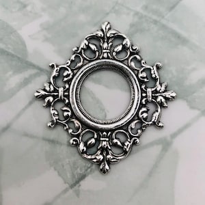 May include: Silver ornate frame with a circular opening in the center. The frame has a decorative design with intricate details.