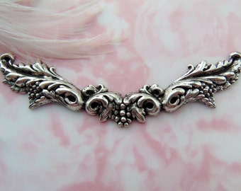 May include: Silver-toned metal embellishment with a decorative, ornate design featuring a grapevine motif. The embellishment is shaped like a curved arch.