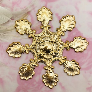 Pode incluir: Um ornamento de floco de neve de metal dourado com um design detalhado que apresenta um motivo circular central e seis pontas com bordas festoneadas.