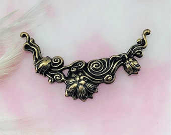 May include: A gold-toned metal embellishment with a floral design. The embellishment features a stylized floral motif with swirling details.