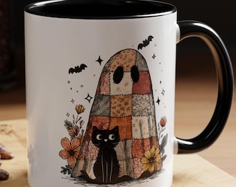May include: White ceramic mug with a black interior and handle. The mug features a whimsical design of a patchwork ghost with a black cat, flowers, and bats, perfect for Halloween or spooky season.