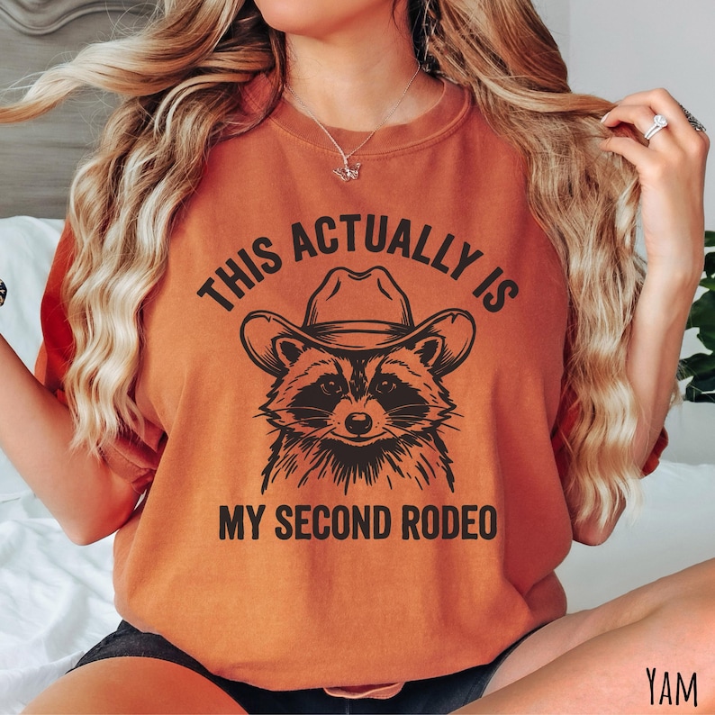 Comfort Colors yam t-shirt with “This Actually Is My Second Rodeo” text and a raccoon wearing a cowboy hat graphic.