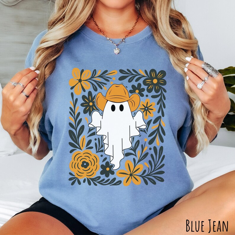 Blue jean Comfort Colors t-shirt featuring a cute ghost wearing a cowboy hat, surrounded by yellow and green floral designs—perfect for fall, Halloween, and western style lovers.