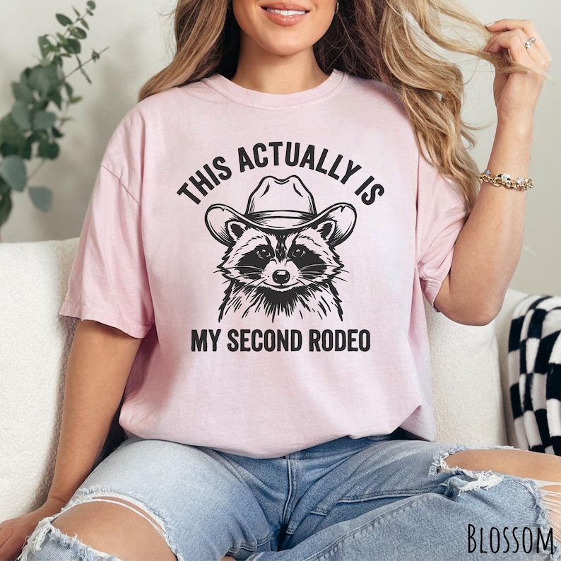 Comfort Colors blossom t-shirt with “This Actually Is My Second Rodeo” text and a raccoon wearing a cowboy hat graphic.