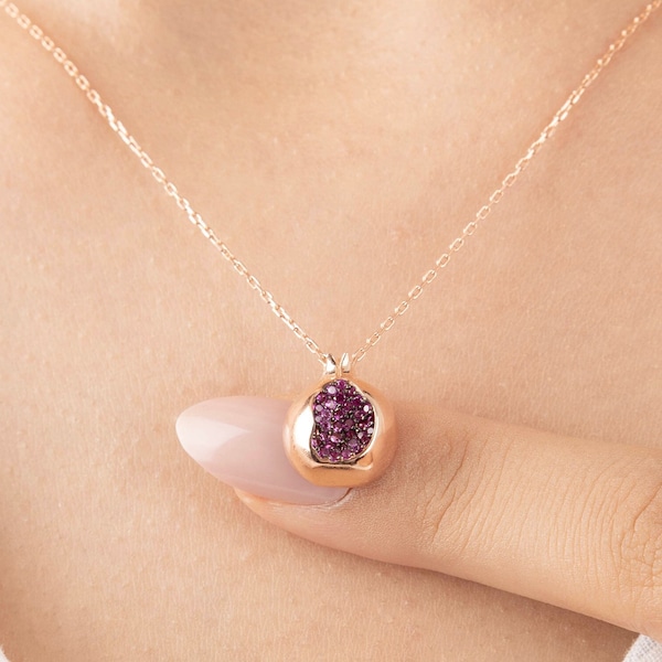 Pode incluir: Um delicado colar de ouro com um pequeno pingente em forma de romã. O pingente é preenchido com pequenas pedras preciosas cor-de-rosa.