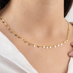 May include: A gold necklace with a delicate chain and small, round charms hanging from it.