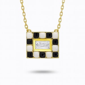 May include: A gold-toned necklace featuring a square pendant with a black and white checkerboard pattern. The center of the pendant holds a rectangular, clear gemstone. The necklace chain is also gold-toned.