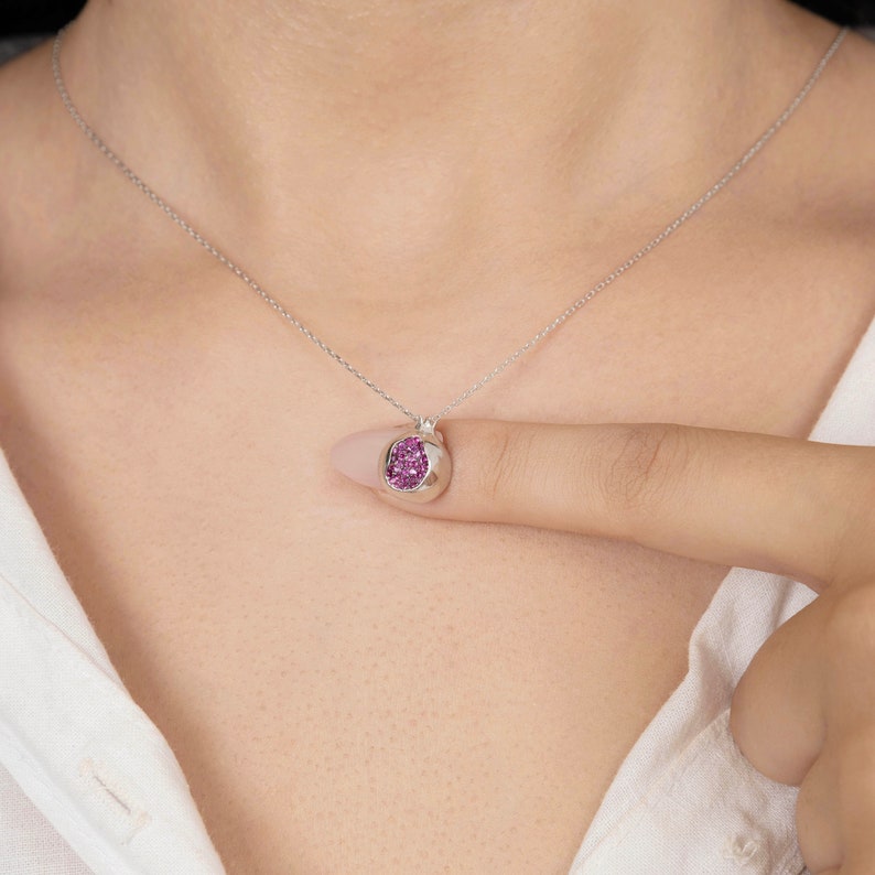 May include: A silver chain necklace with a small pendant featuring a round, pink gemstone.