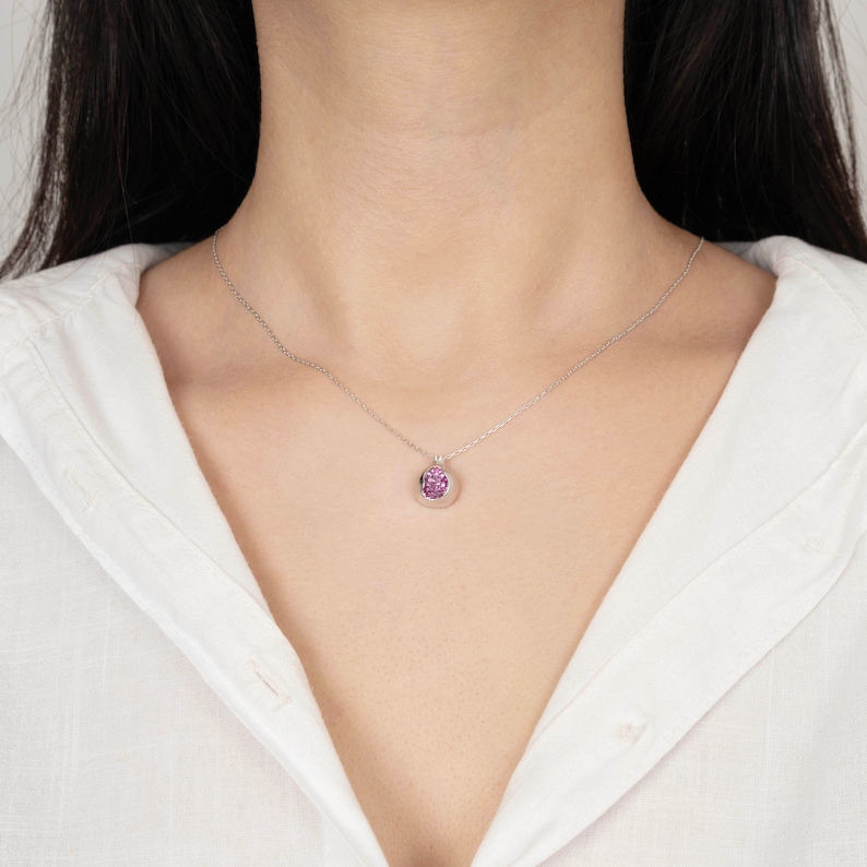 May include: A silver chain necklace with a small pendant featuring a pink gemstone.