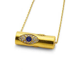 May include: A gold-colored pendant necklace featuring a cylindrical charm. The charm is adorned with a blue gemstone center, surrounded by clear crystals, and set in a gold-tone metal. The necklace chain is also gold-colored.