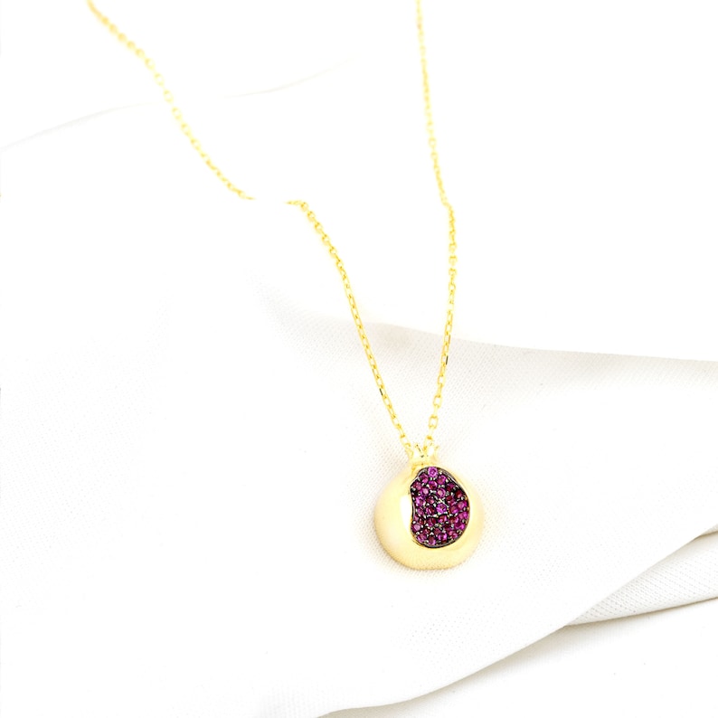 May include: A gold chain necklace with a round pendant featuring a pink gemstone design.
