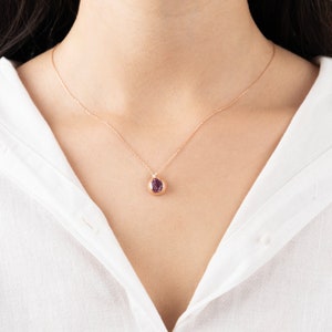 May include: A delicate gold necklace with a small pendant featuring a purple gemstone. The pendant is round and has a smooth, polished finish.
