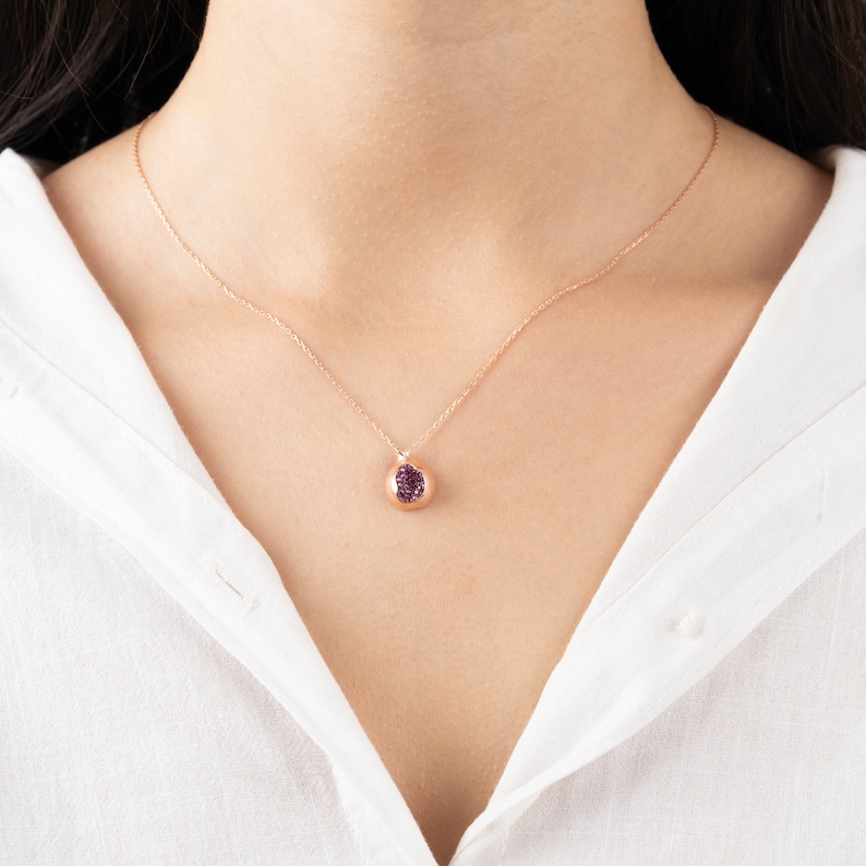 May include: A delicate gold necklace with a small pendant featuring a purple gemstone. The pendant is round and has a smooth, polished finish.