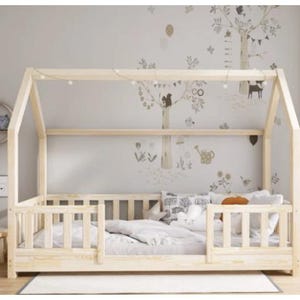 Peut inclure: Un lit en bois en forme de maison avec un matelas blanc et une couverture blanche et grise. Le lit est doté d'une barrière en bois blanc autour du matelas et d'un auvent en bois blanc. Le lit se trouve dans une pièce avec un mur blanc et un tapis gris au sol.