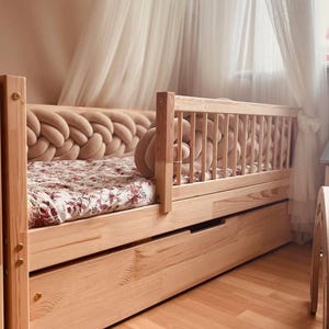 Peut inclure: Un cadre de lit en bois clair avec un matelas à motifs floraux. La tête de lit présente un design tressé et le lit dispose d'un tiroir coulissant. Un rideau transparent est suspendu en arrière-plan, créant une atmosphère douce et accueillante.
