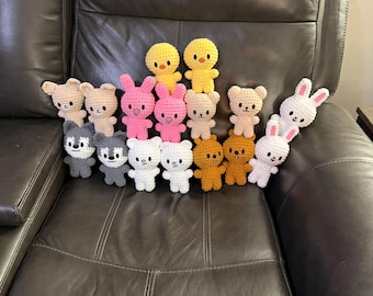 May include: A collection of handmade crochet stuffed animals, including bears, bunnies, chicks, and wolves. The toys are in various colors, such as pink, white, yellow, and brown. The toys are arranged on a dark brown leather recliner.