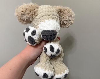 May include: A handmade crochet plush dog toy crafted from soft, beige and white yarn. The stuffed animal features long, fluffy ears, a dark gray nose, and white paws with dark gray circular pads. The texture is thick and plush throughout the body.