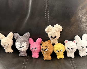 May include: A collection of handmade crochet animal figures, including bunnies, a wolf, a bear, and a chick. The figures are in various colors such as beige, gray, pink, and yellow. Each figure has embroidered facial features.